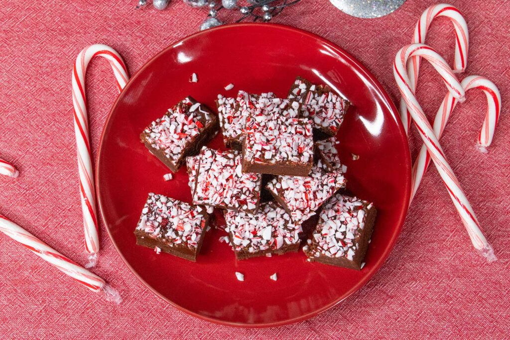 Peppermint fudge on a red plate with scattered candy canes.