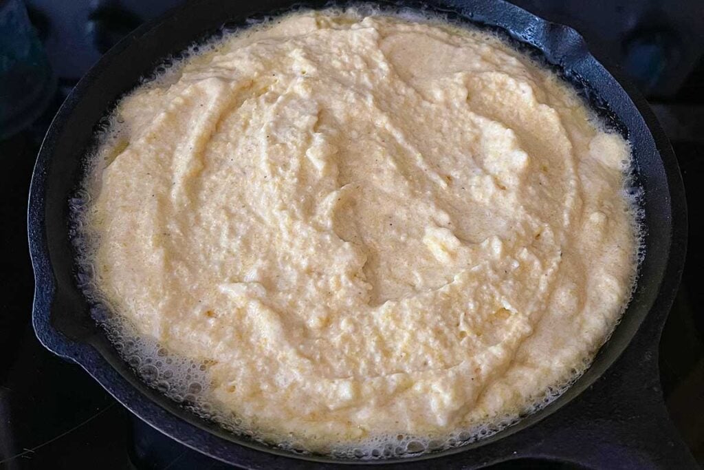 Cornbread mixture sizzling in a cast iron skillet