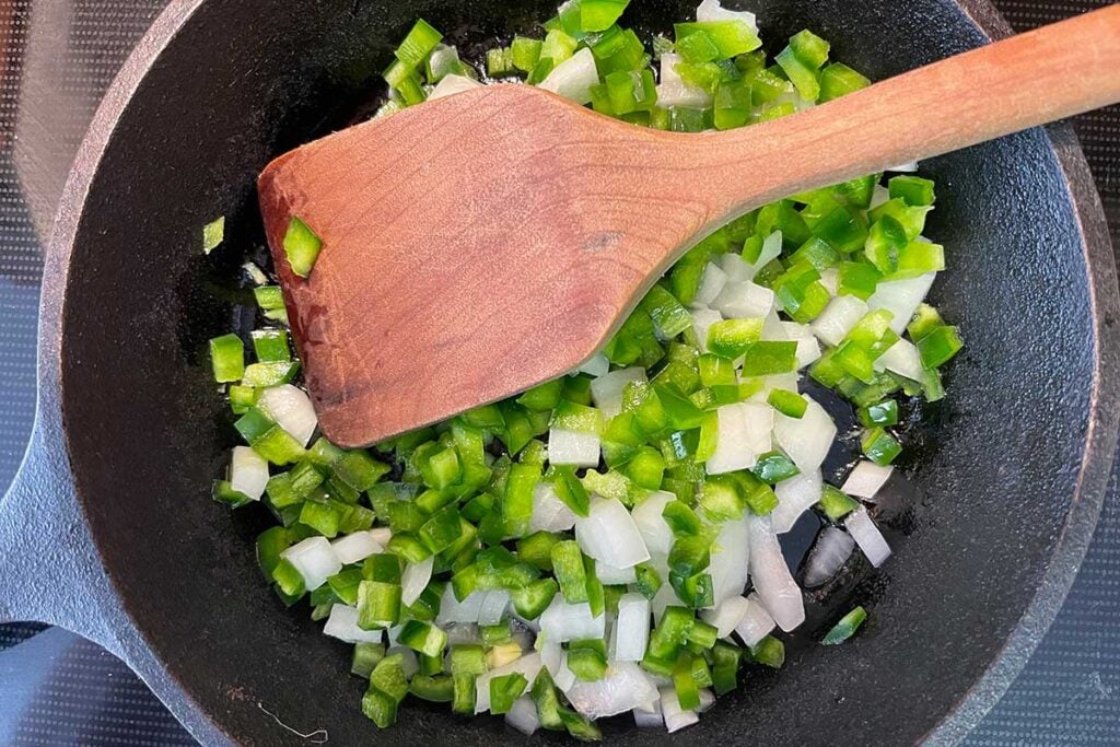 Green pepper, onion, and jalapeno cooking in a cast iron skillet