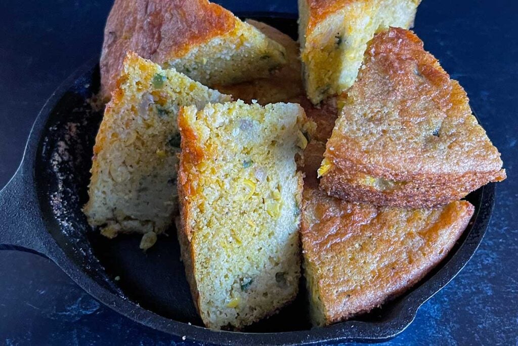 Creole cornbread slices stacked in a cast iron skillet.
