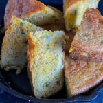 Creole cornbread slices stacked in a cast iron skillet.