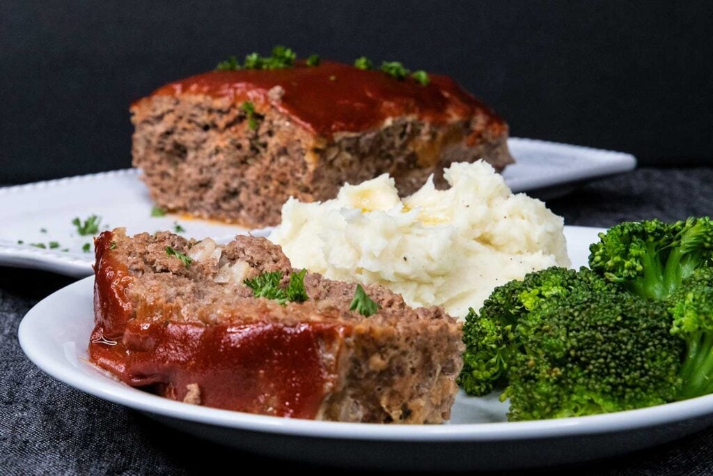 Meatloaf with mashed potatoes and broccoli on a white plate.