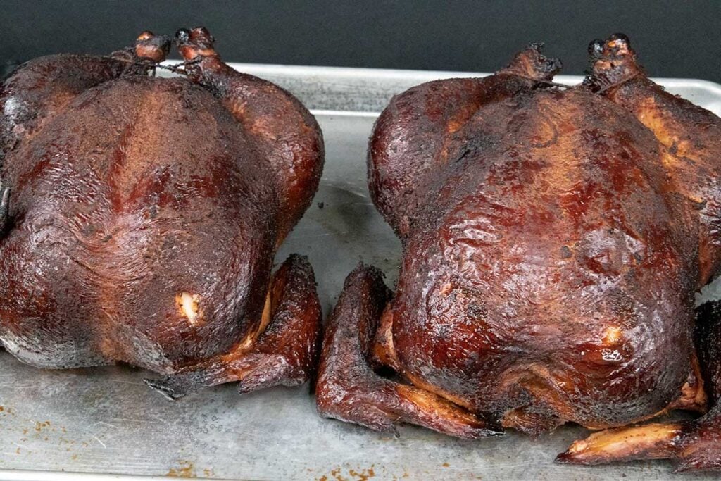 Two whole smoked chickens on a baking sheet