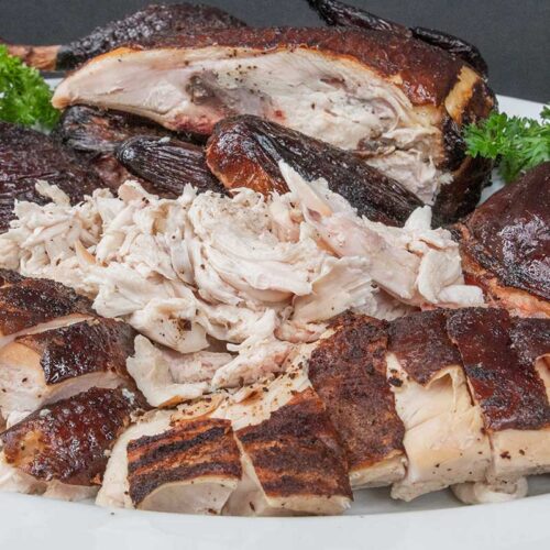 Smoked chicken cut up on a white platter garnished with whole parsley.