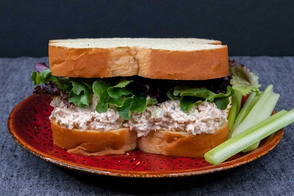 Smoked chicken salad sandwich with celery as a garnish on a red plate.