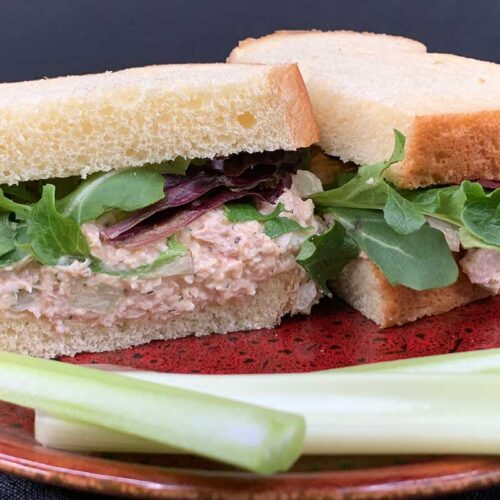 Smoked chicken salad sandwich on a red plate with celery sticks.