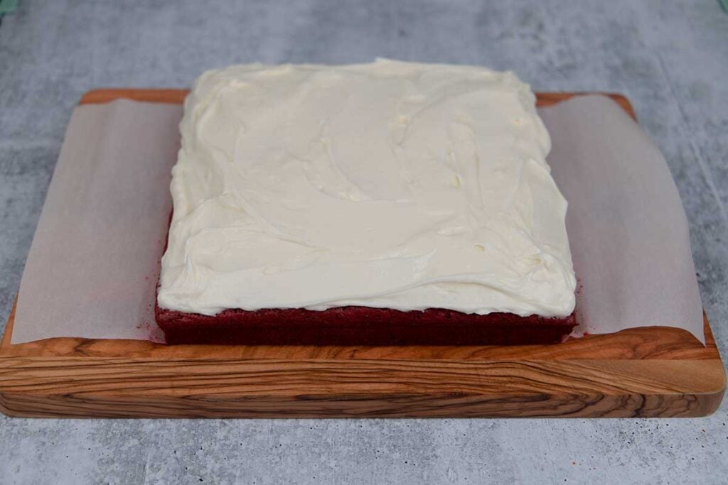 Frosted red velvet brownies on a wooden board.