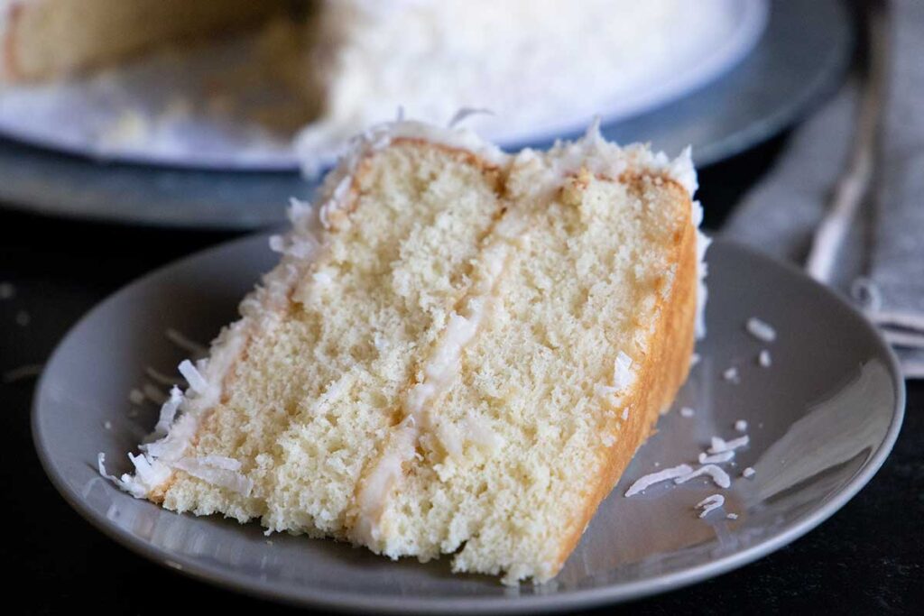 A slice of coconut cake on light colored plate.
