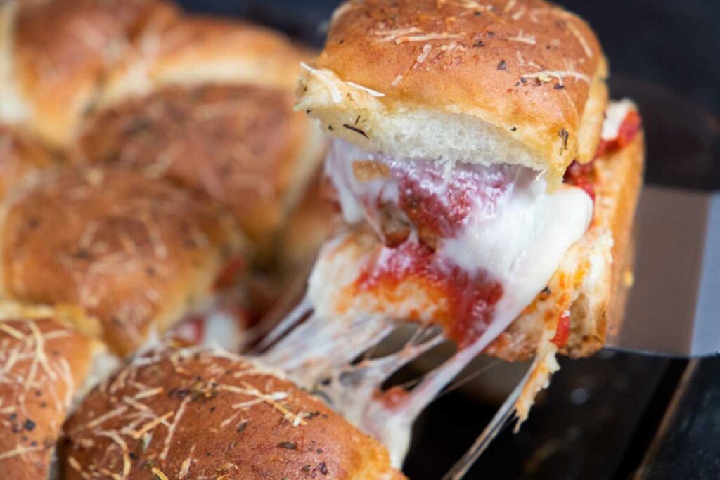 A meatball slider being removed from the 9x13 inch baking dish.