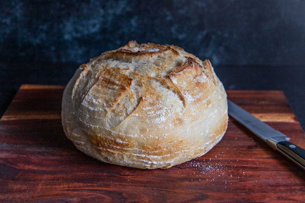 A boule of sourdough on a cutting board with a knife.