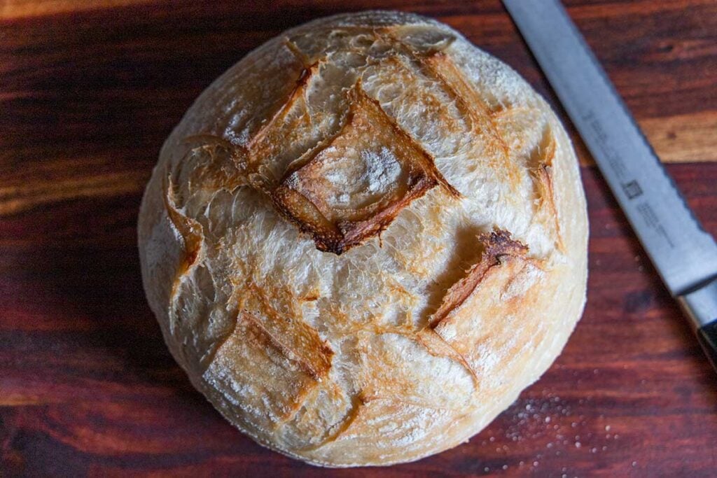 A boule of sourdough on a cutting board with a bread knife.