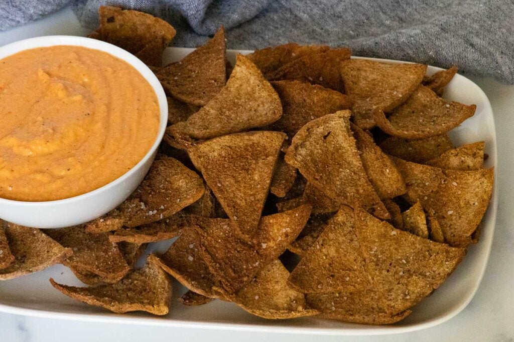 Baked pita chips with a bowl of dip on a white platter