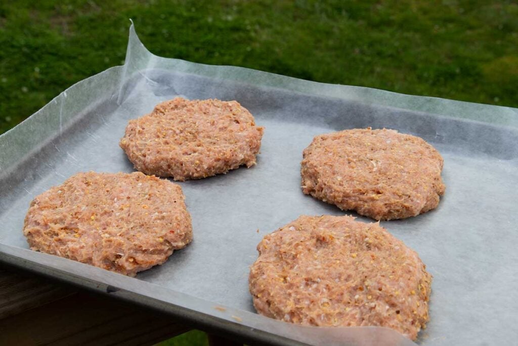 Four uncooked turkey burgers on a parchment lined baking sheet.