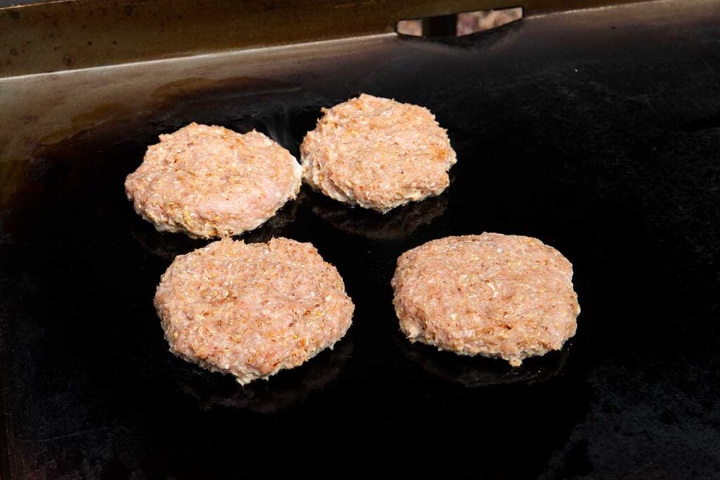 Four turkey burgers cooking on a flat top griddle