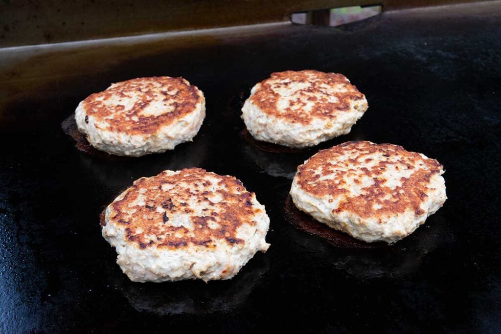 Four turkey burgers cooking on a flat top griddle