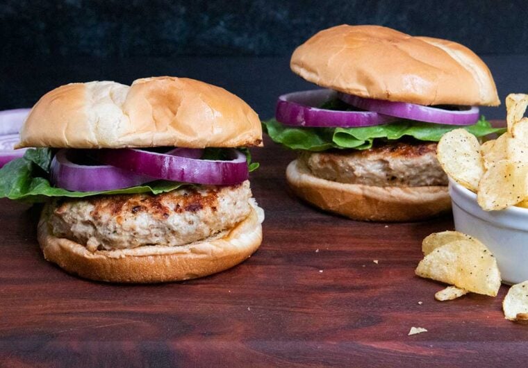 Two turkey burgers with lettuce and red onion on a cutting board