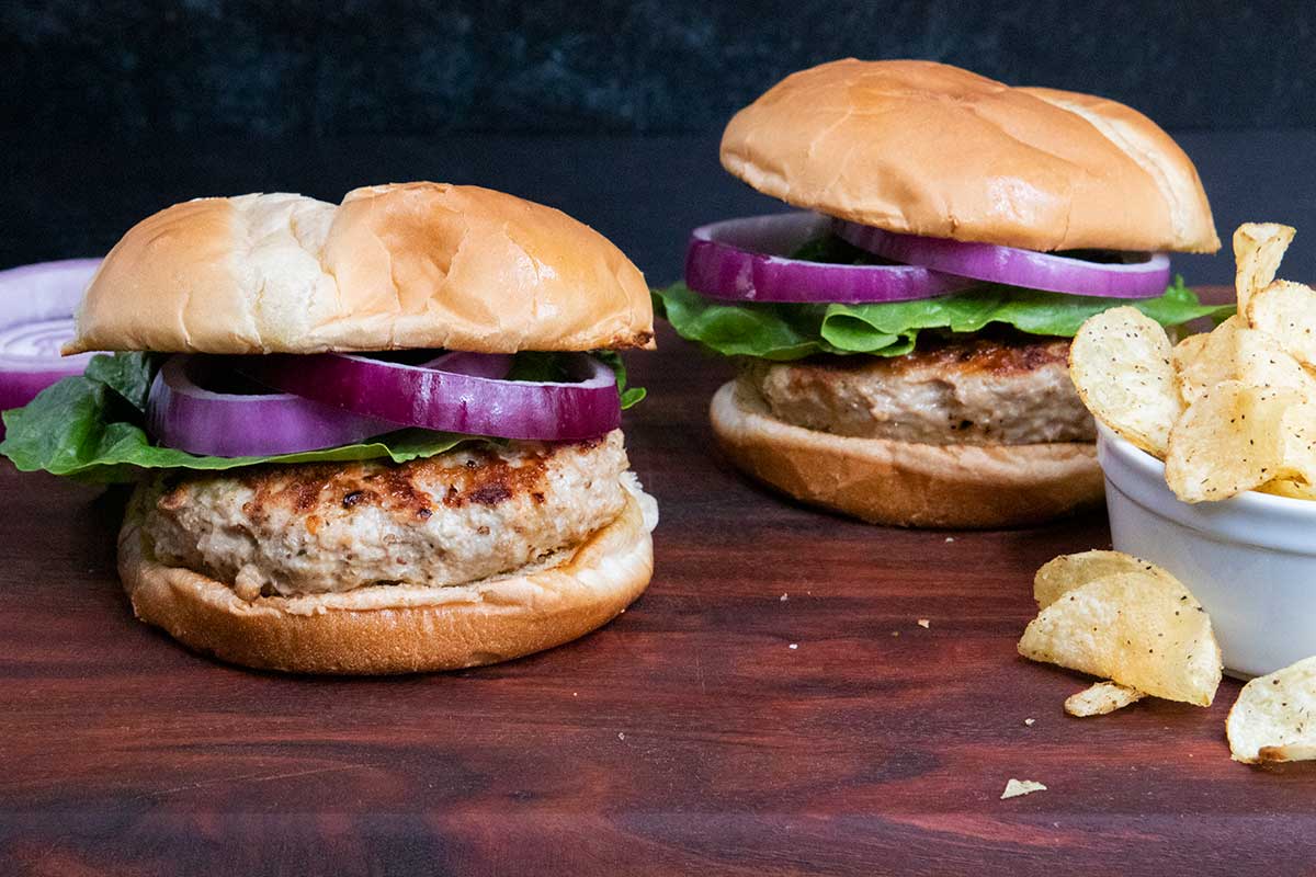 Two turkey burgers with lettuce and red onion on a cutting board