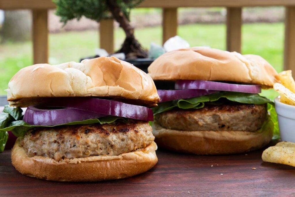 Two turkey burgers with lettuce and red onion on a cutting board.