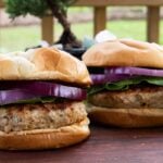 Two turkey burgers with lettuce and red onion on a cutting board.