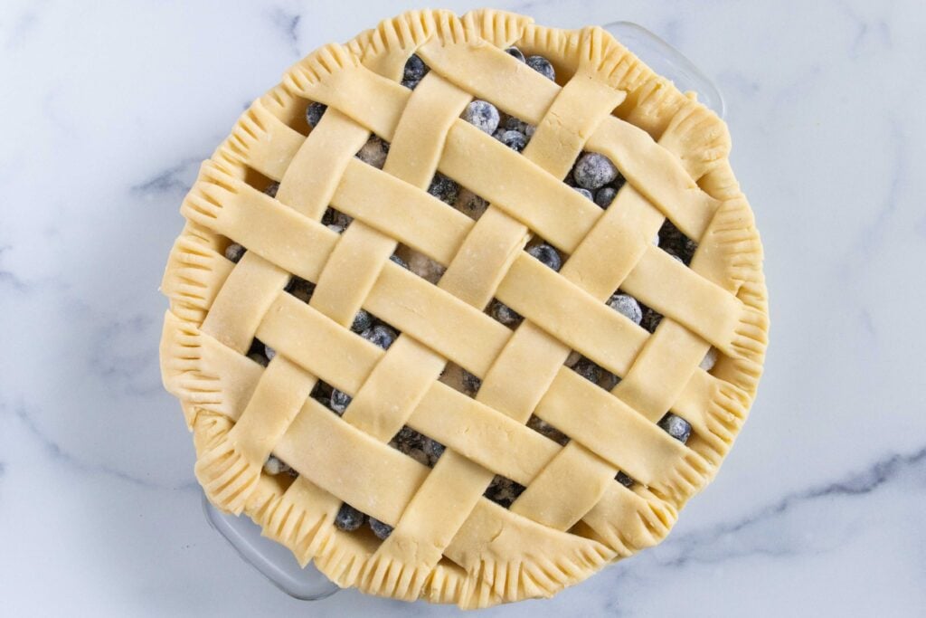 Unbaked blueberry pie with a lattice crust on a light surface.