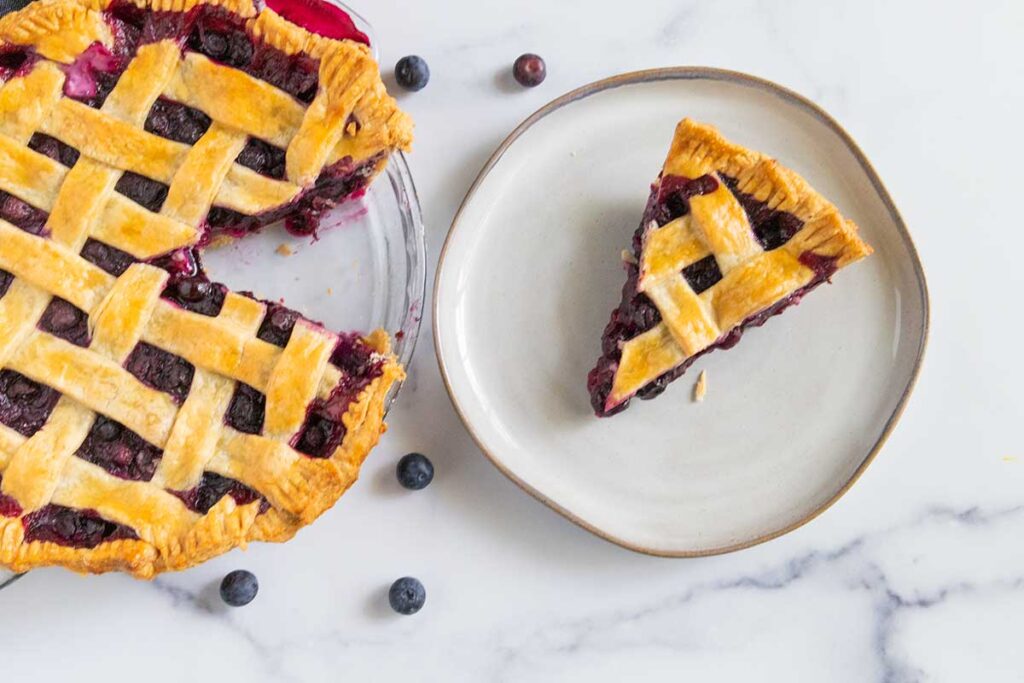 blueberry pie on a white plate with the rest of the pie off to the side.