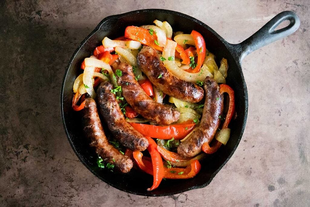 grilled beer brats with onions and peppers in a cast iron skillet