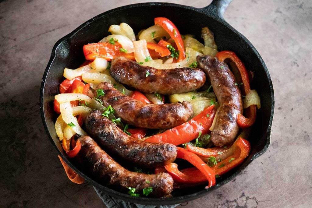 beer brats with peppers and onions, cooked, in a cast iron skillet