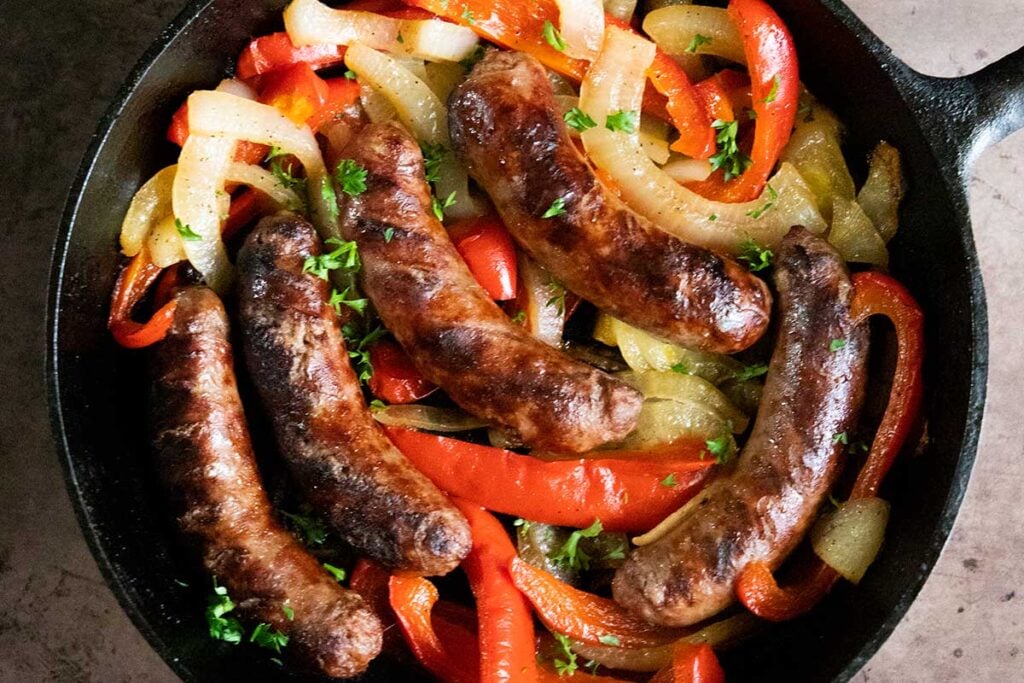 Beer brats with peppers and onions in a cast iron skillet.