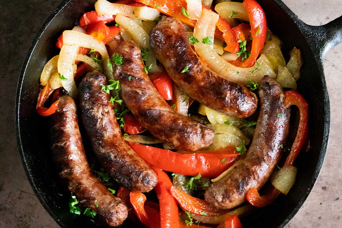 beer brats with peppers and onions in a cast iron skillet