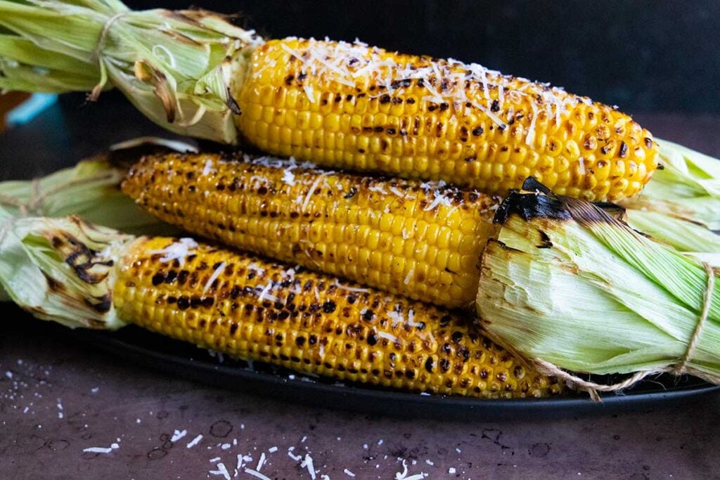 Grilled corn on the cob on a black plate.