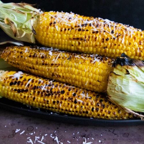 Grilled corn on the cob on a black plate.