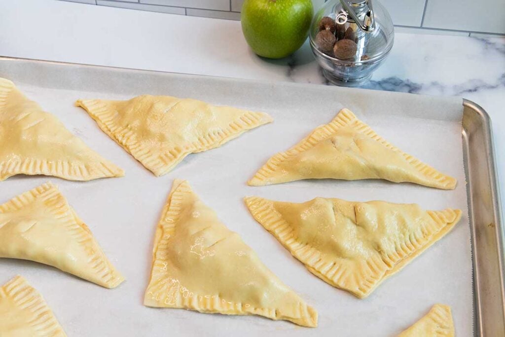 Formed apple turnovers on a baking sheet.