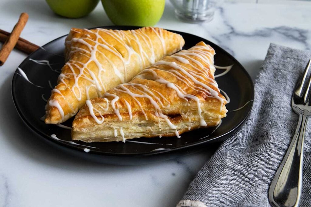 Puff pastry apple turnovers on a black plate.