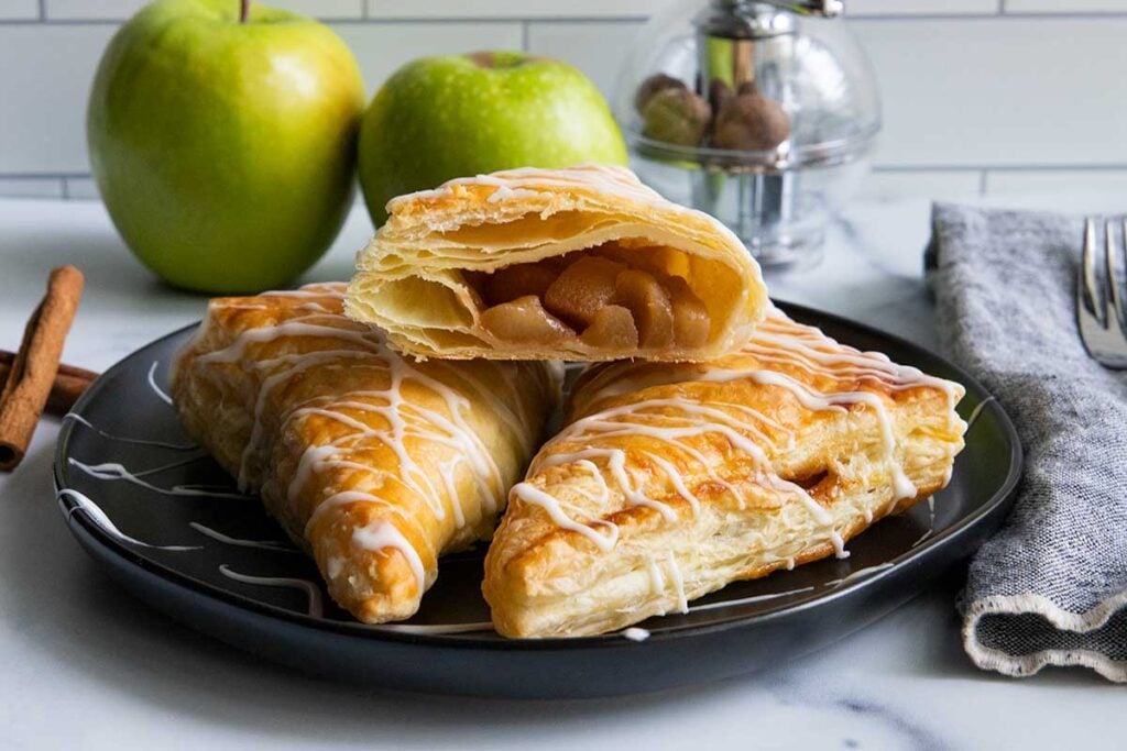Apple turnovers on black plate with green apples in the background.