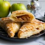 Apple turnovers on black plate with green apples in the background.