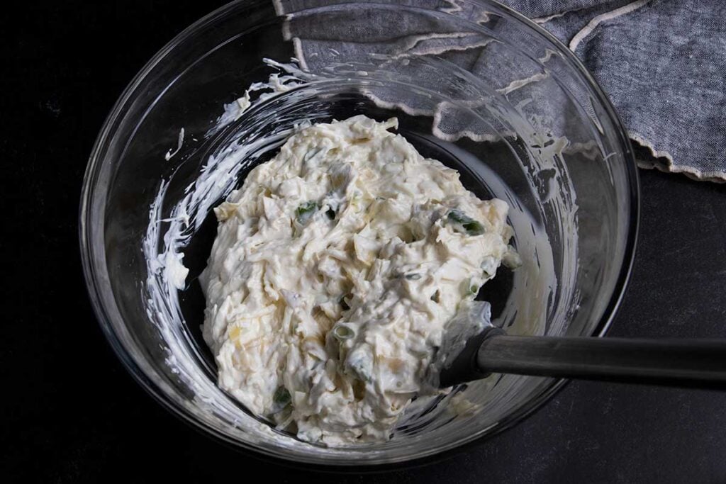 Artichoke dip ingredient mixture in a glass bowl.