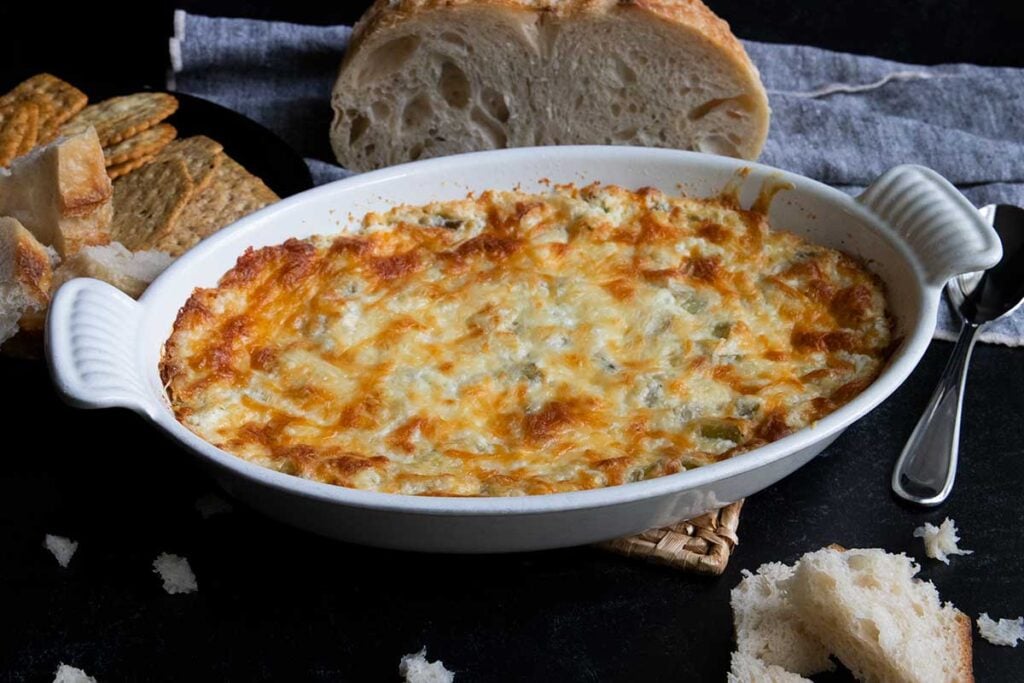 Artichoke dip in a white oval baking dish with bread in the background.