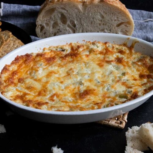 Artichoke dip in a white oval baking dish with bread in the background.