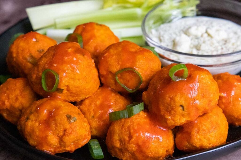 Buffalo chicken meatballs with celery and blue cheese on a black plate.