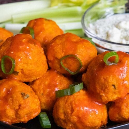 Buffalo chicken meatballs with celery and blue cheese on a black plate.