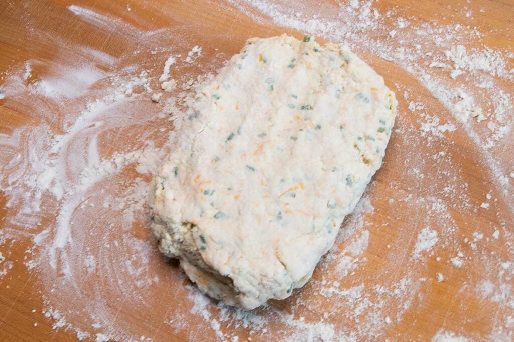 Cheddar chive biscuit dough on wooden cutting board.