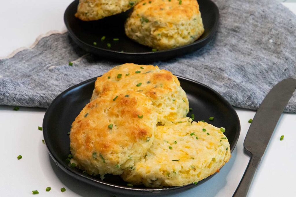 Cheddar chive biscuits on black plates.