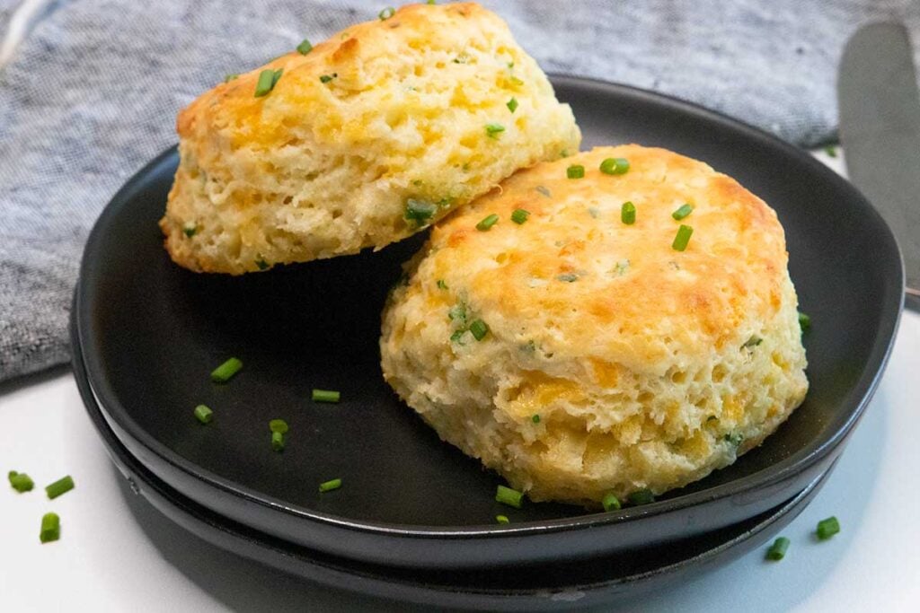 Cheddar chive biscuits on a black plate.
