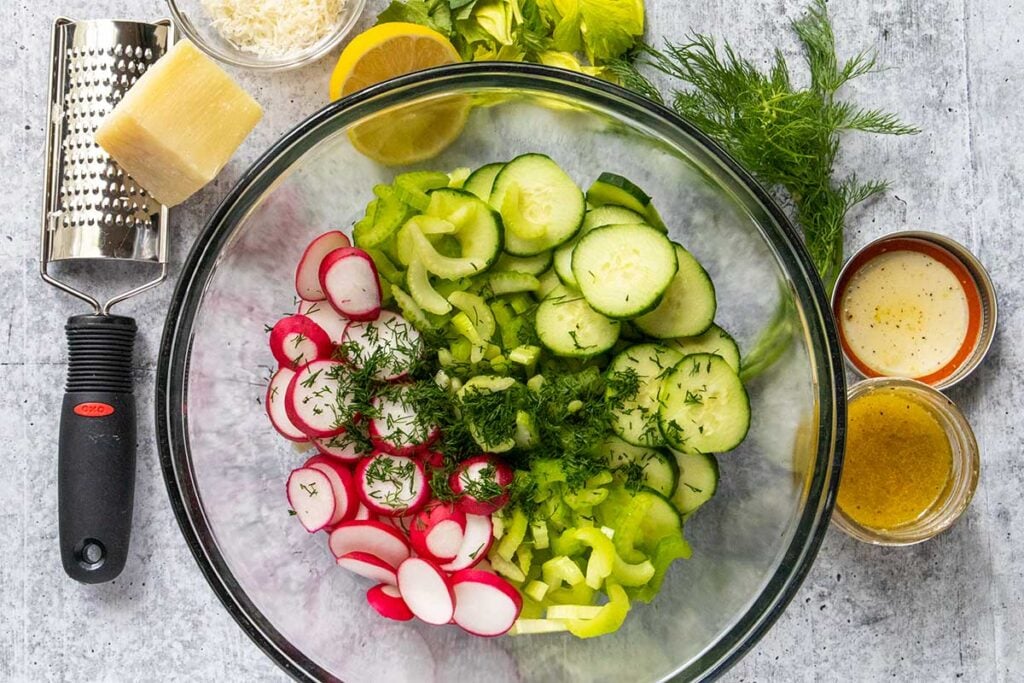 sliced cucumbers, radishes, celery, and chopped fresh dill in a glass bowl