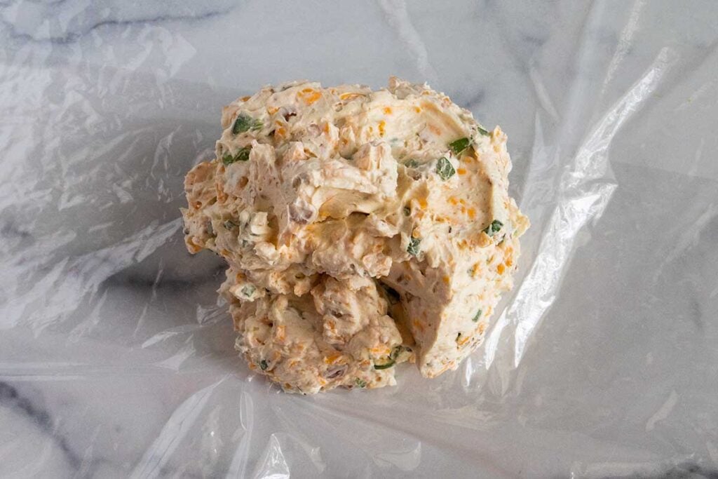 Jalapeno popper cheese ball with out the topping in a sheet of plastic wrap.