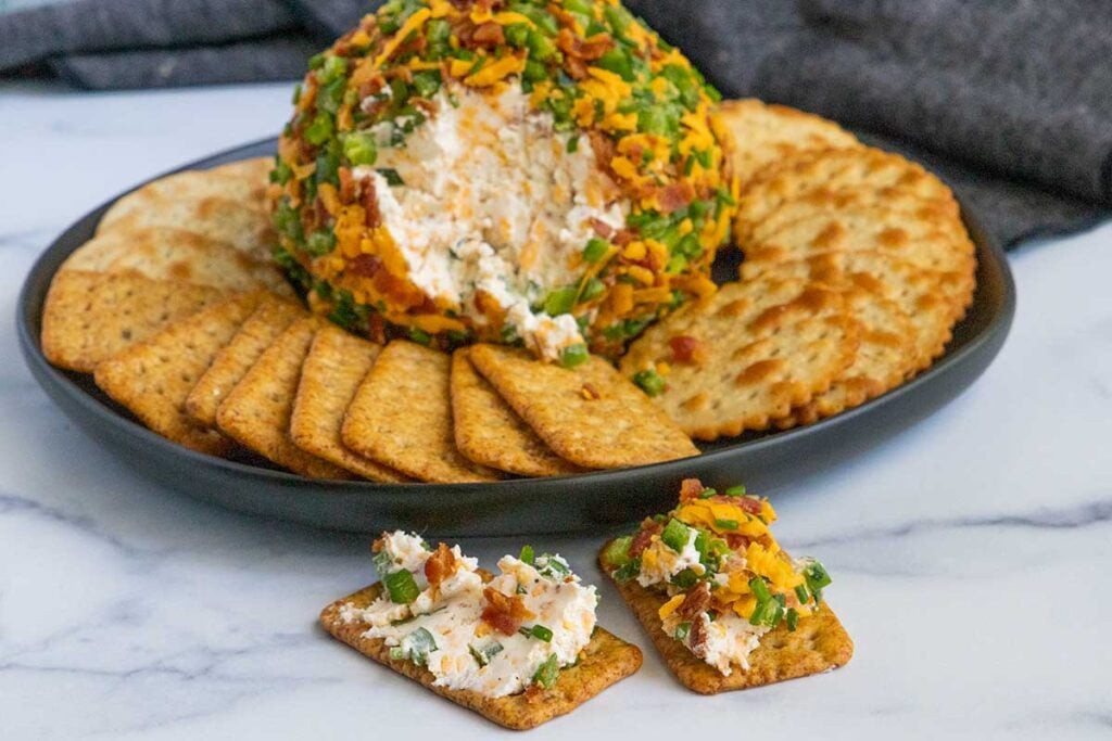 Jalapeno popper cheese ball with crackers on a dark plate.