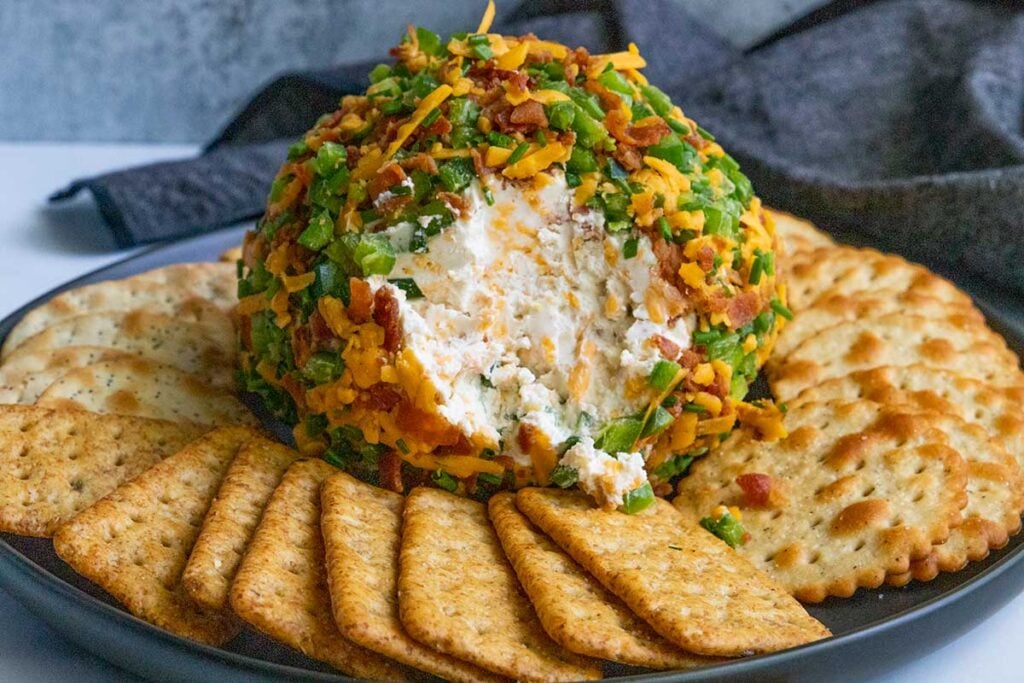 Jalapeno Popper Cheese Ball on a black plate with crackers.