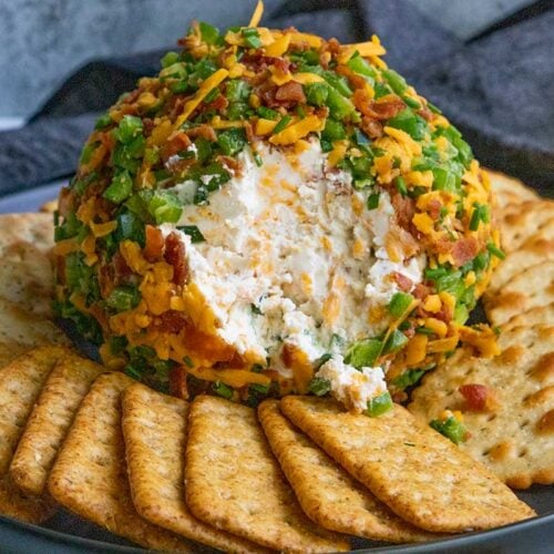 Jalapeno Popper Cheese Ball on a black plate with crackers.