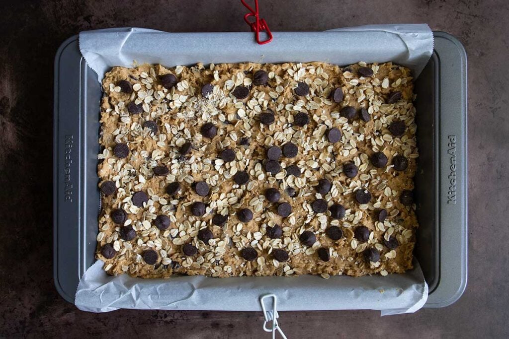 oatmeal chocolate chip cookie bar dough in a parchment lined baking pan