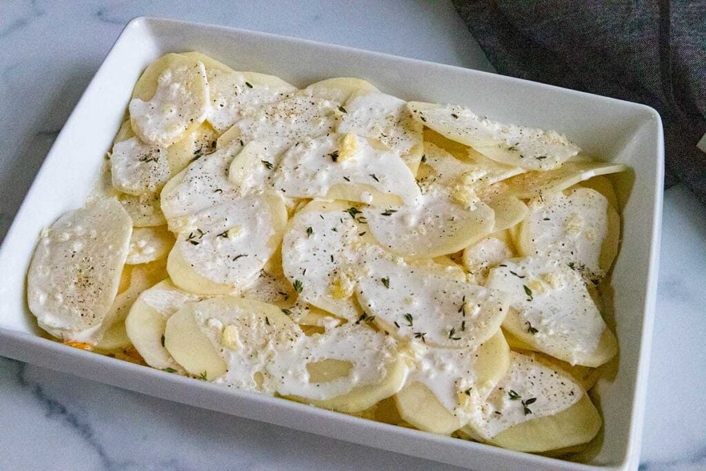 Sliced raw potatoes with cream sauce on top in a baking dish.